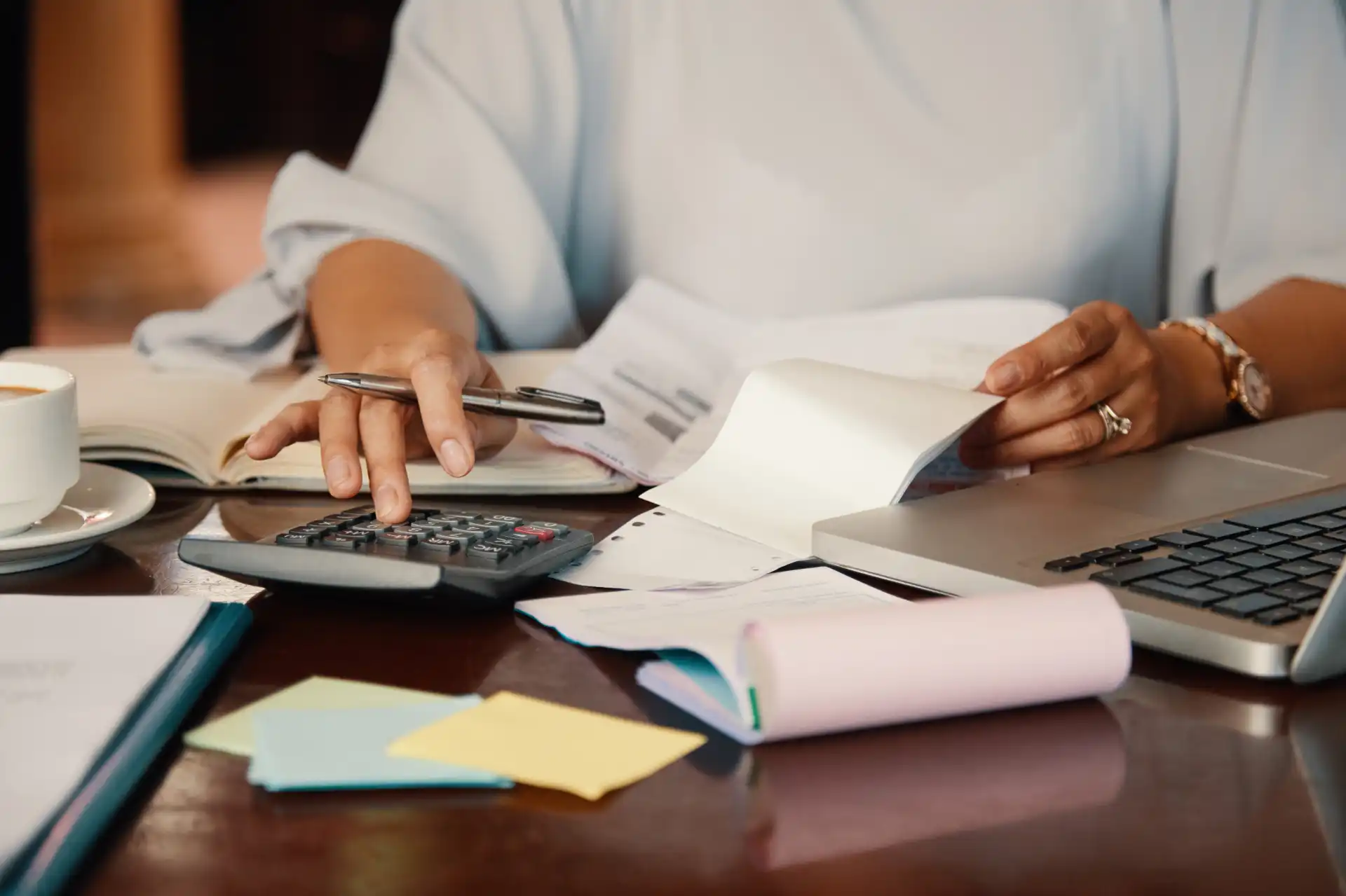 Pessoa analisando documentos financeiros e calculando capital de giro em ambiente de escritório, com laptop, relatórios e papelada na mesa.